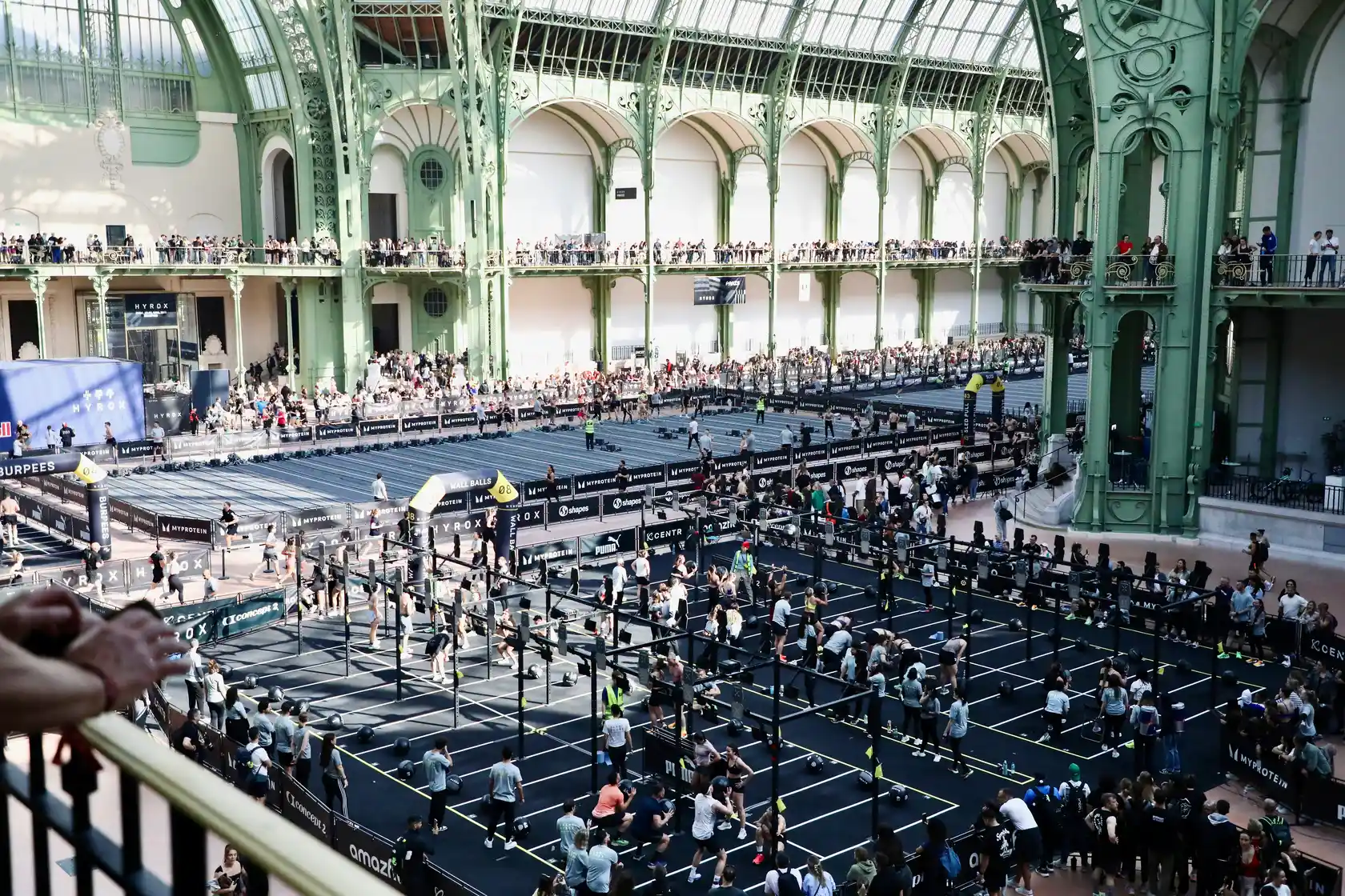 Athletes competing in a Hyrox fitness race inside a large arena with workout stations and running lanes